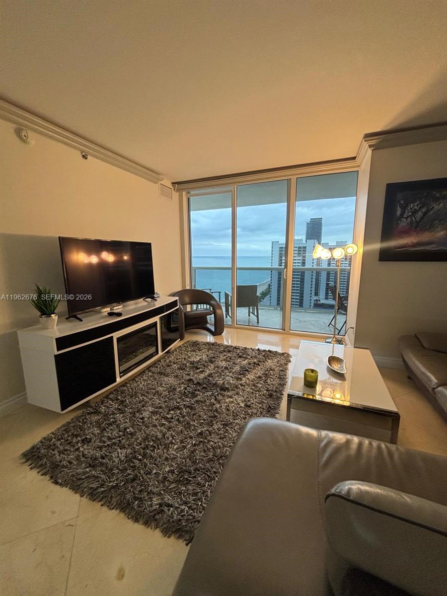 A living room features a television console, a shaggy rug, and a balcony overlooking the ocean — 1830 S OCEAN DR # 2004, Hallandale Beach FL 33009, HALLANDALE BEACH, FL