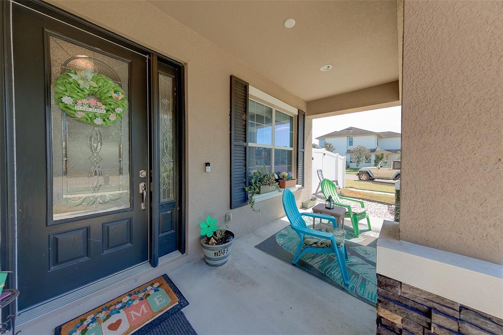 A covered front porch features a dark door, two blue chairs, and a welcome mat — 7405 70TH AVENUE N, PINELLAS PARK, FL