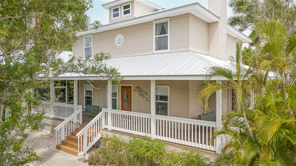 A two-story house with beige siding, a metal roof, and a wrap-around front porch — 740 W VIRGINIA AVENUE, PUNTA GORDA, FL