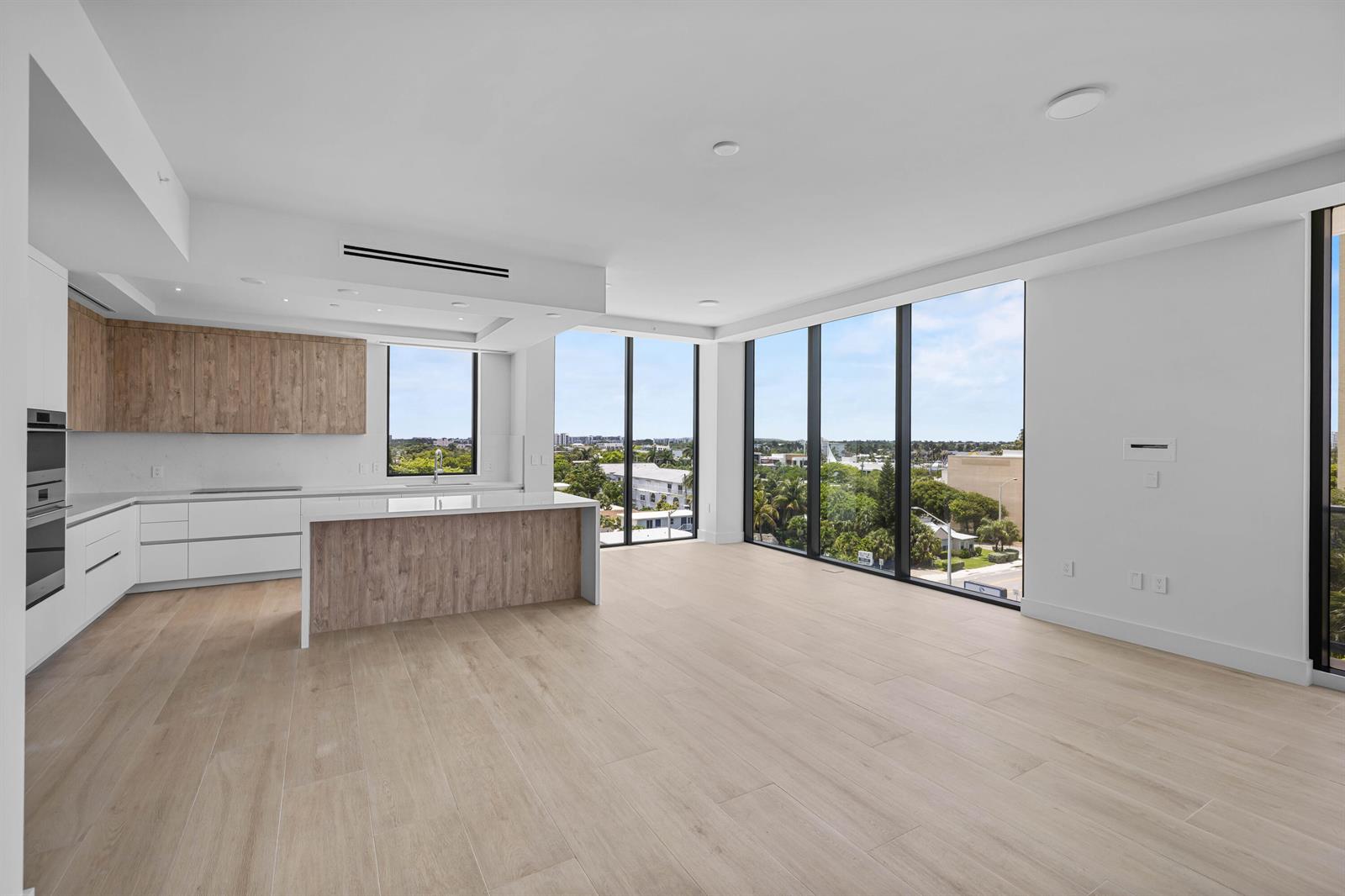 A modern kitchen and living area with light wood flooring, white cabinetry, and floor-to-ceiling windows — 305 Briny Avenue # 506, Pompano Beach FL 33062, POMPANO BEACH, FL