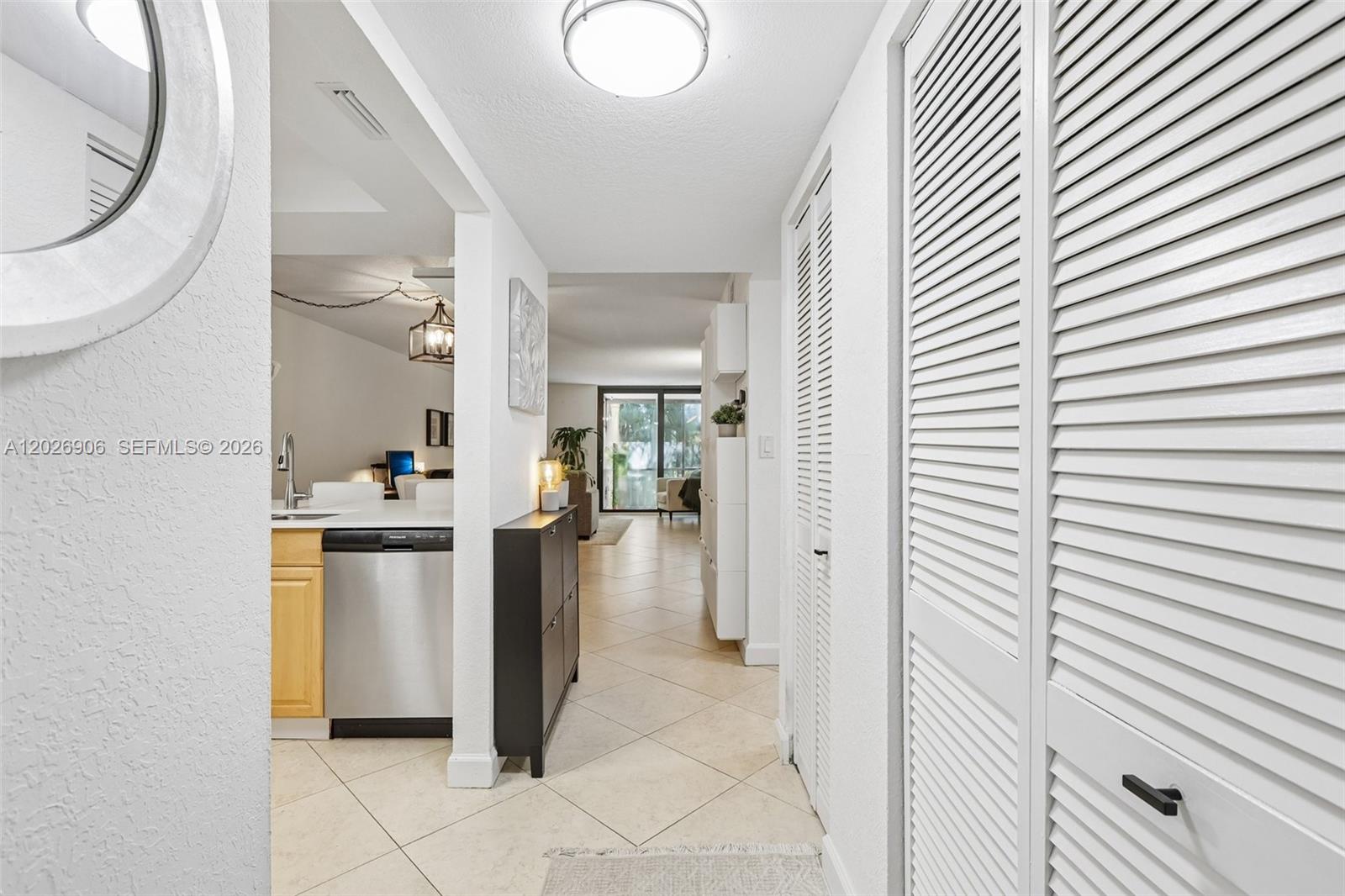 A hallway with white louvered closet doors leads to an open kitchen and living area — 400 Commodore Dr # 206, Plantation FL 33325, PLANTATION, FL