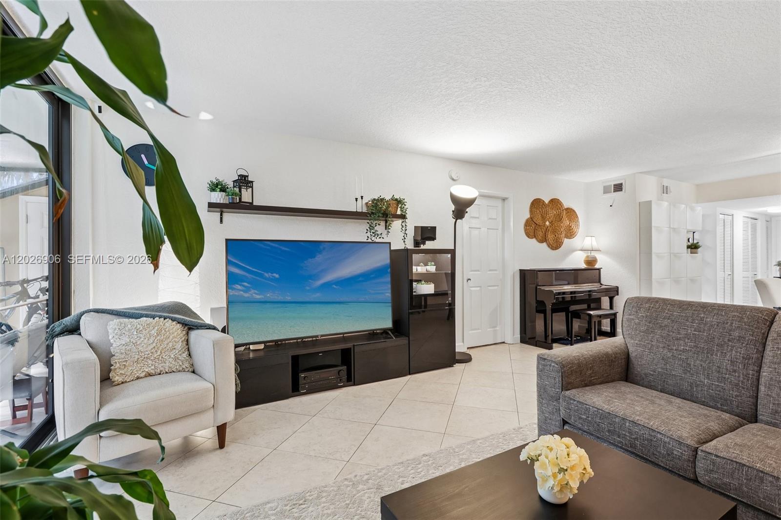 A living room features a television console, a piano, and tile flooring — 400 Commodore Dr # 206, Plantation FL 33325, PLANTATION, FL