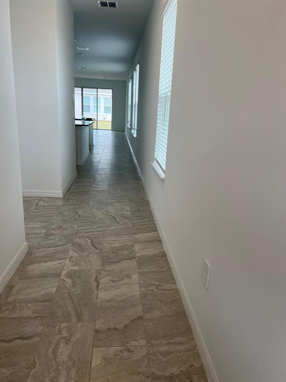 A long hallway with light-colored tile flooring leads toward an open kitchen and sliding doors — 5274 KILDARE PLACE, ST CLOUD, FL