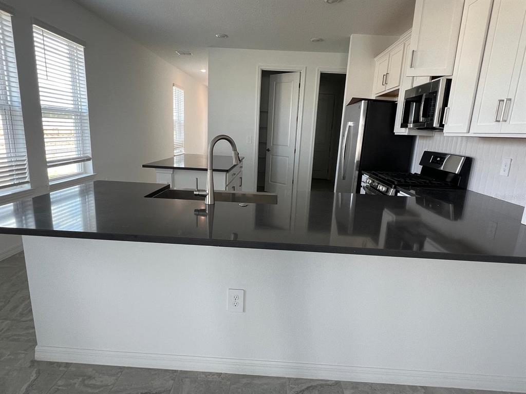 A kitchen island with a dark countertop and sink faces white cabinets and appliances — 5274 KILDARE PLACE, ST CLOUD, FL