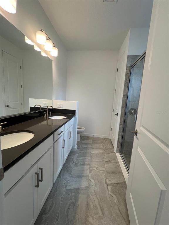 A bathroom features a double vanity with dark countertops, white cabinets, and a glass-enclosed shower — 5274 KILDARE PLACE, ST CLOUD, FL