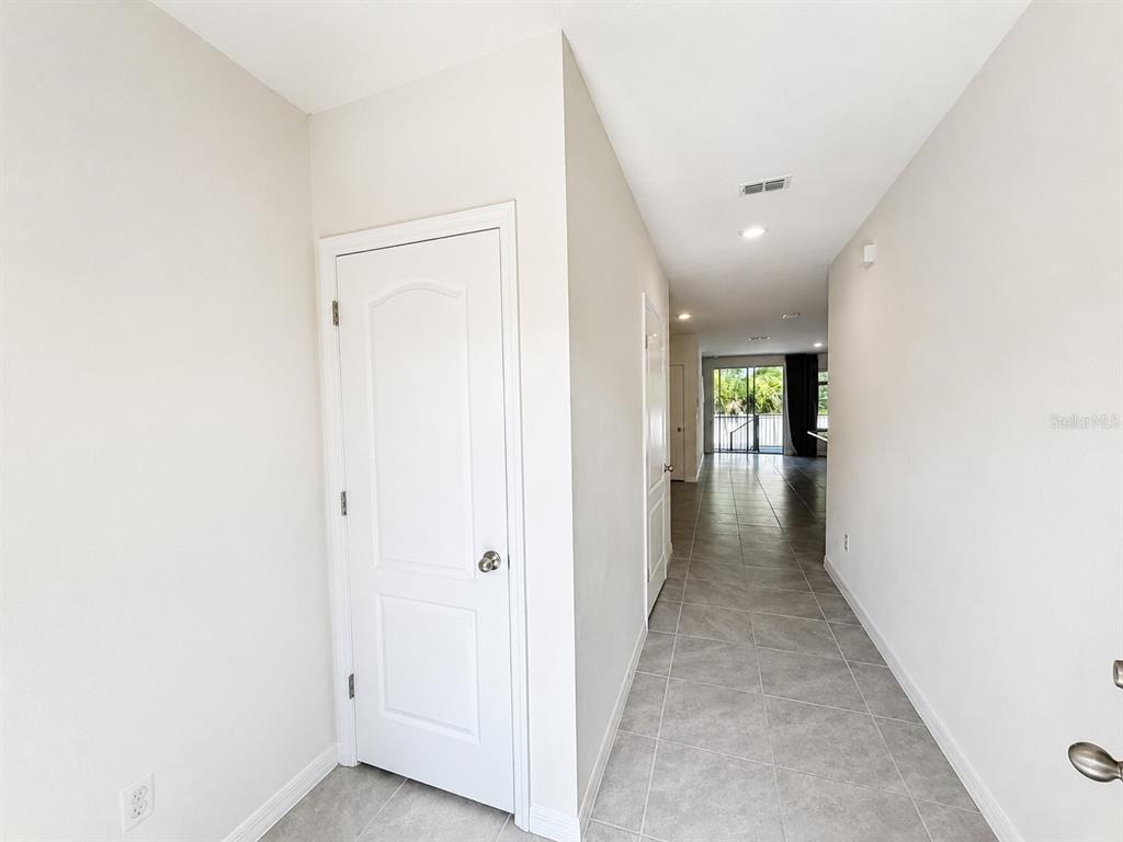 A hallway with light-colored tile flooring leads toward a glass sliding door at the end — 13 BELLA OAKS DR DRIVE, PORT ORANGE, FL