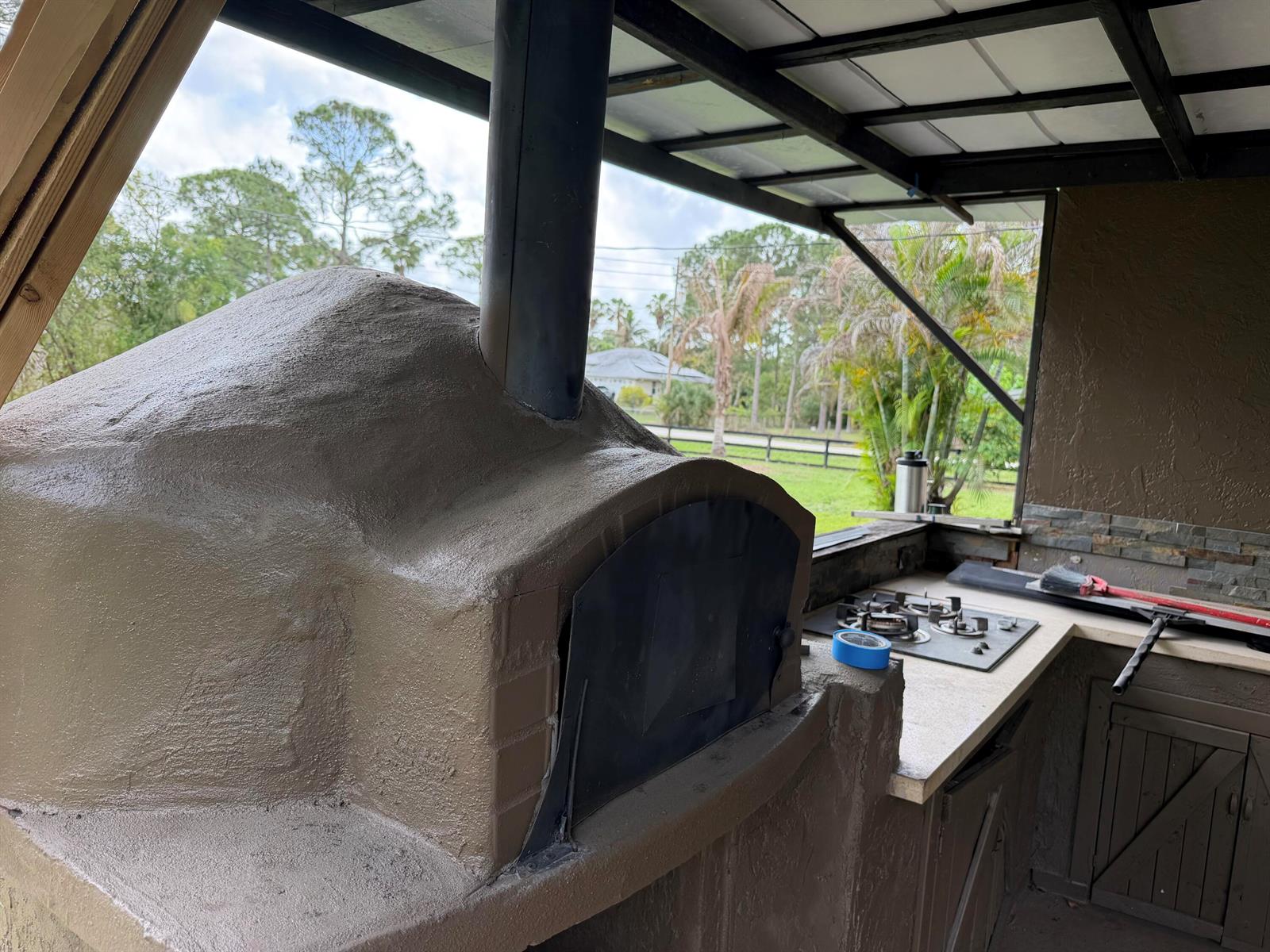 An outdoor kitchen features a stucco pizza oven with a chimney and a gas cooktop — 14307 N 80th Ln Lane N, FL 33470, FL
