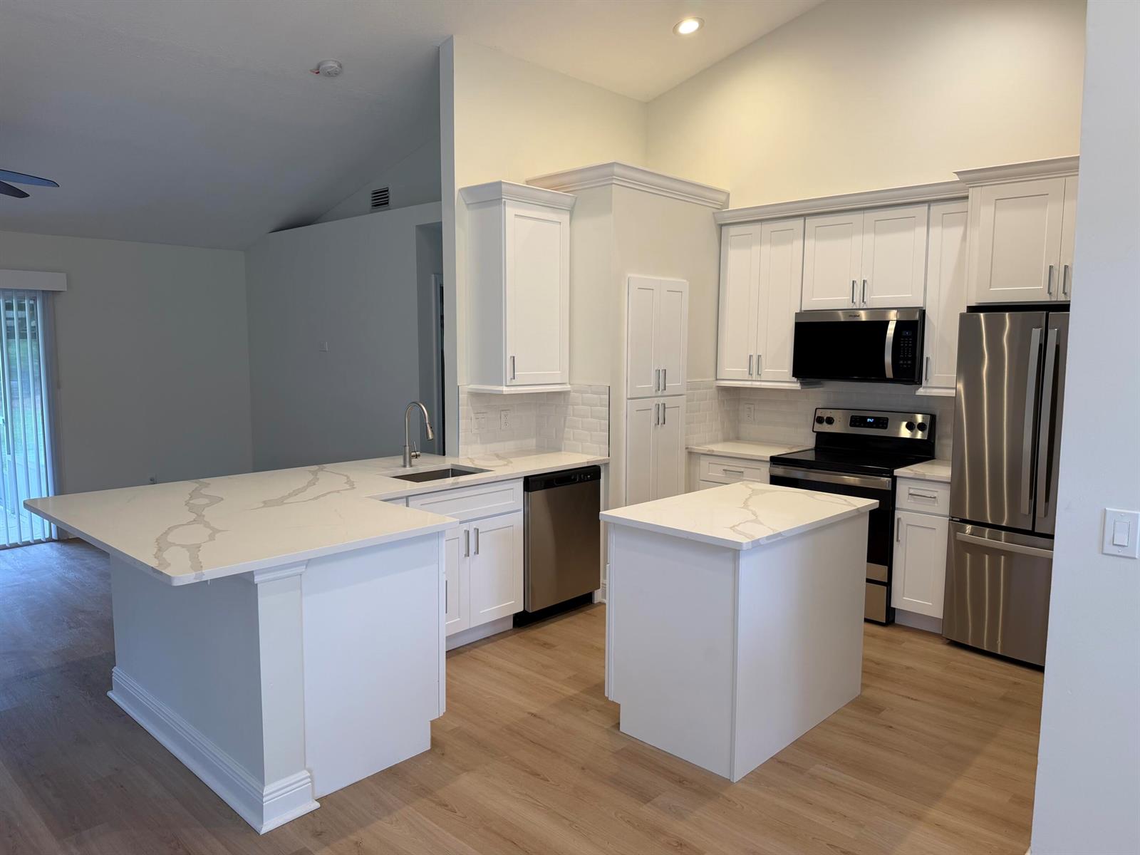 A kitchen features white cabinets, stainless steel appliances, and a quartz-topped island and peninsula — 14307 N 80th Ln Lane N, FL 33470, FL