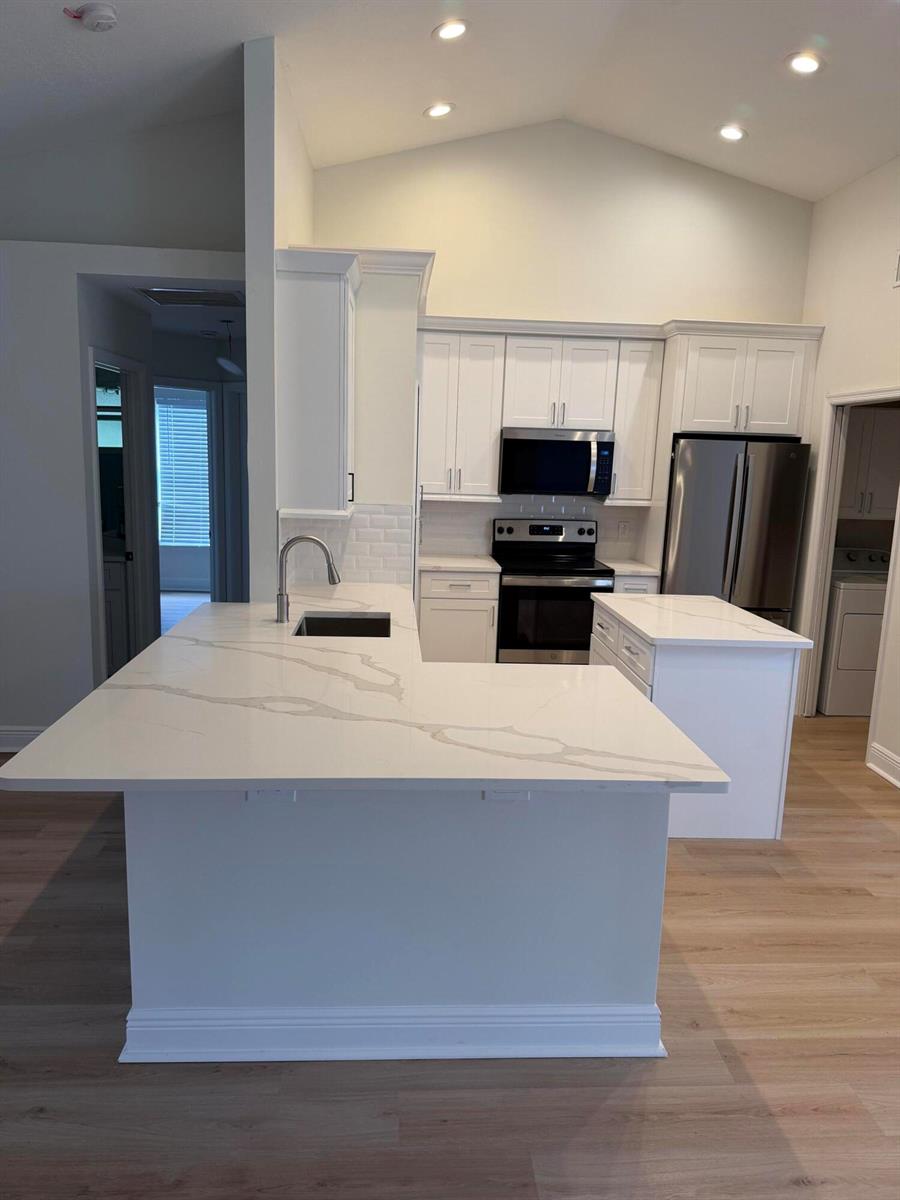 A modern kitchen features white cabinets, quartz countertops, stainless steel appliances, and light wood flooring — 14307 N 80th Ln Lane N, FL 33470, FL