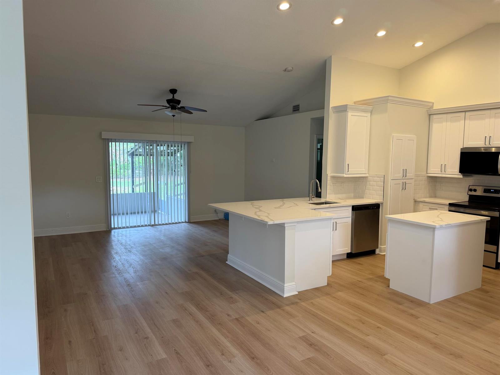 An open-concept kitchen with white cabinets, marble-look countertops, and light wood flooring — 14307 N 80th Ln Lane N, FL 33470, FL