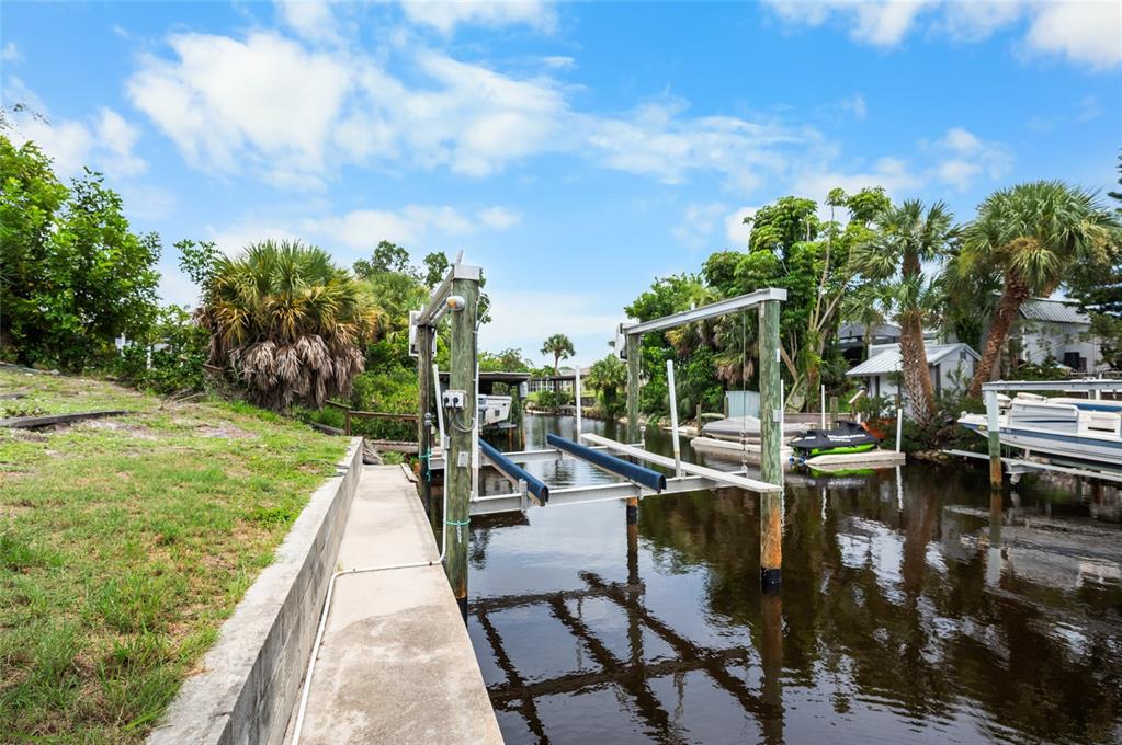 A concrete walkway leads to a boat lift on a canal lined with tropical vegetation — 2113 GEORGIA AVENUE, ENGLEWOOD, FL