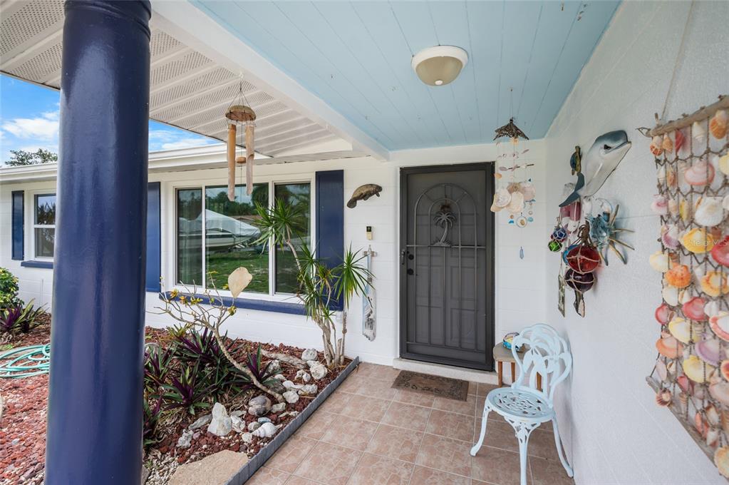 A covered front porch features a blue ceiling, a dark screen door, and coastal decor — 2113 GEORGIA AVENUE, ENGLEWOOD, FL