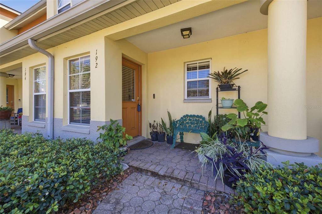 A yellow house exterior features a front porch with a brick walkway and potted plants — 192 COQUINA BAY DRIVE, ST PETERSBURG, FL