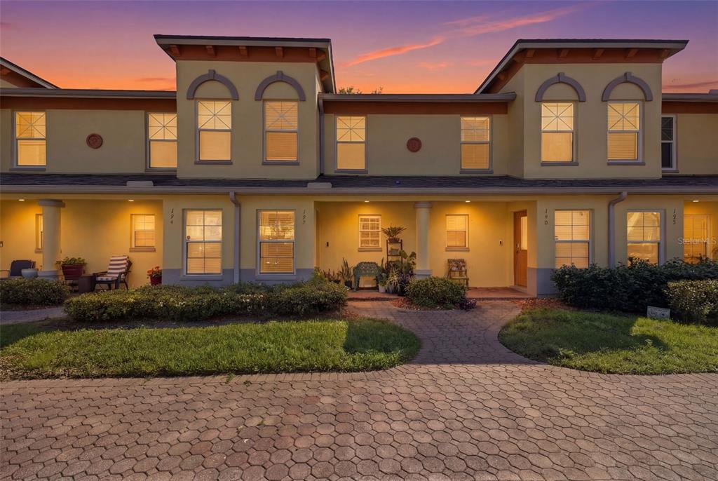 A two-story townhouse exterior with a paved driveway, arched windows, and warm sunset lighting — 192 COQUINA BAY DRIVE, ST PETERSBURG, FL