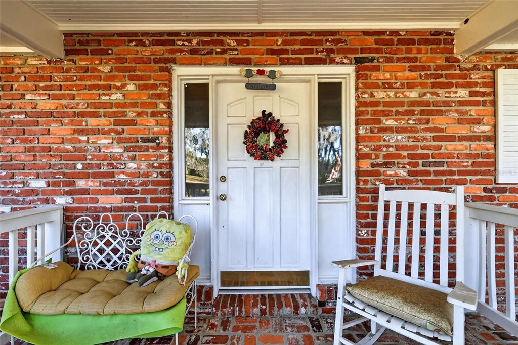A front porch features a brick wall, a white door with a wreath, and two chairs — 2230 SW 87TH PLACE, OCALA, FL