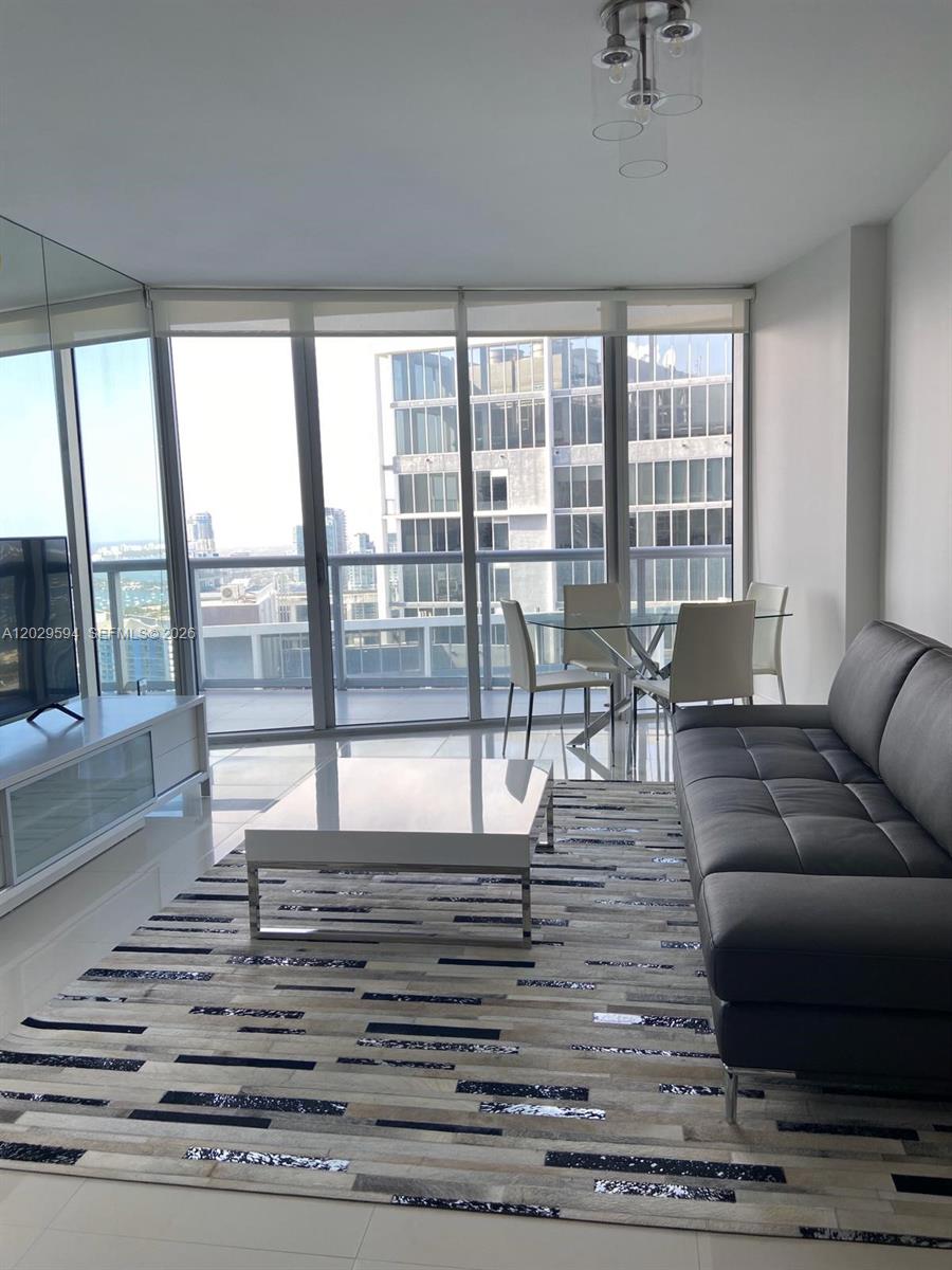 A modern living room features a grey sofa, white coffee table, and floor-to-ceiling windows — 495 Brickell Ave # 5706, Miami FL 33131, MIAMI, FL