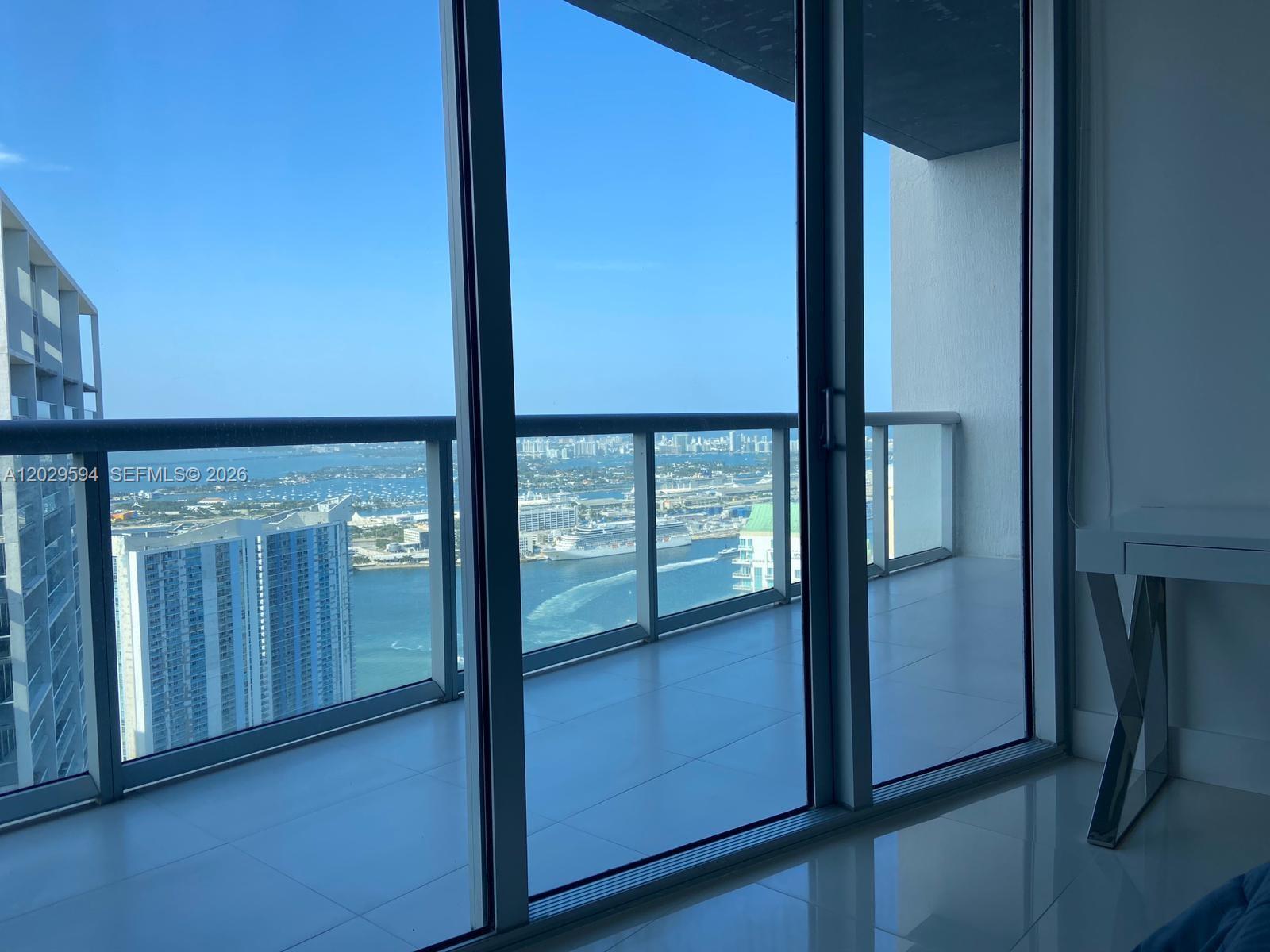 A balcony with glass railings overlooks a harbor with cruise ships and city buildings — 495 Brickell Ave # 5706, Miami FL 33131, MIAMI, FL
