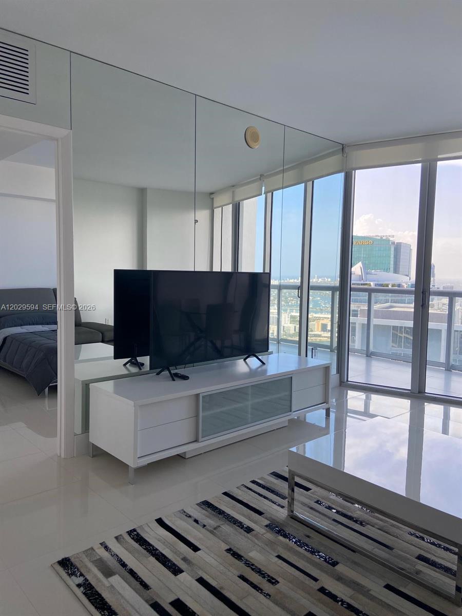 A living room features a white media console, a television, and a mirrored wall — 495 Brickell Ave # 5706, Miami FL 33131, MIAMI, FL