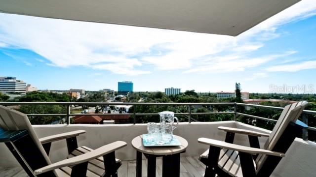 A balcony with two wooden chairs and a small table overlooking a city skyline — 1400 1ST AVENUE W UNIT 806, BRADENTON, FL