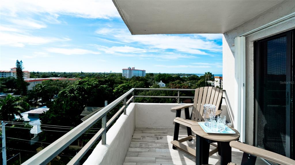 A balcony with a wooden chair and small table overlooks a coastal landscape — 1400 1ST AVENUE W UNIT 806, BRADENTON, FL