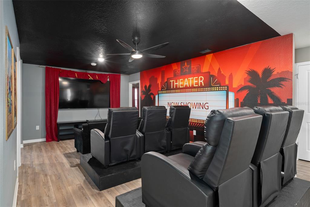 A home theater room features tiered seating, a large television, and a mural on the wall — 3723 LANA AVENUE, DAVENPORT, FL