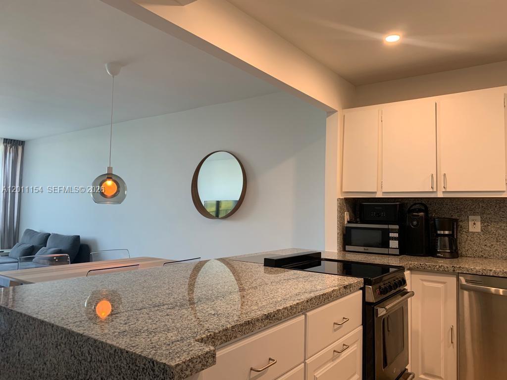 A kitchen with white cabinets, granite countertops, and a stove overlooks a dining area — 780 NE 69th St # 506, Miami FL 33138, MIAMI, FL