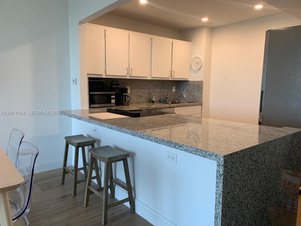 A kitchen features white cabinets, granite countertops, a breakfast bar with stools, and stainless appliances — 780 NE 69th St # 506, Miami FL 33138, MIAMI, FL