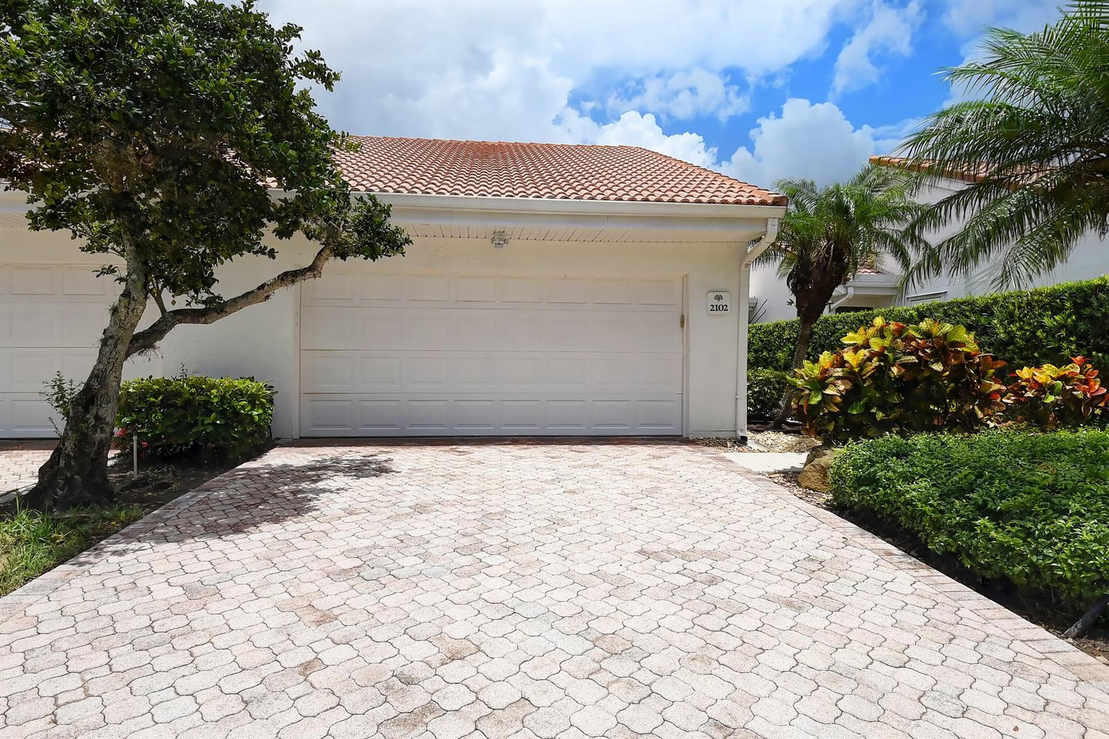 A white garage with a tiled roof and a paved driveway sits beside a tree — 19550 Sawgrass Drive # 2102, Boca Raton FL 33434, BOCA RATON, FL