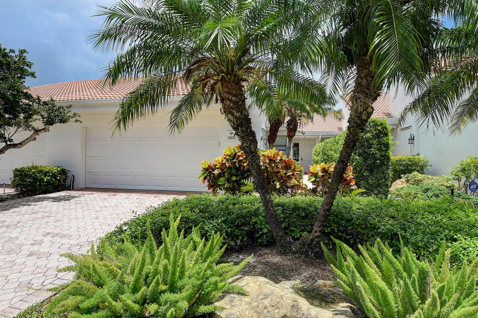A white house with a two-car garage, a paved driveway, and palm trees in front — 19550 Sawgrass Drive # 2102, Boca Raton FL 33434, BOCA RATON, FL