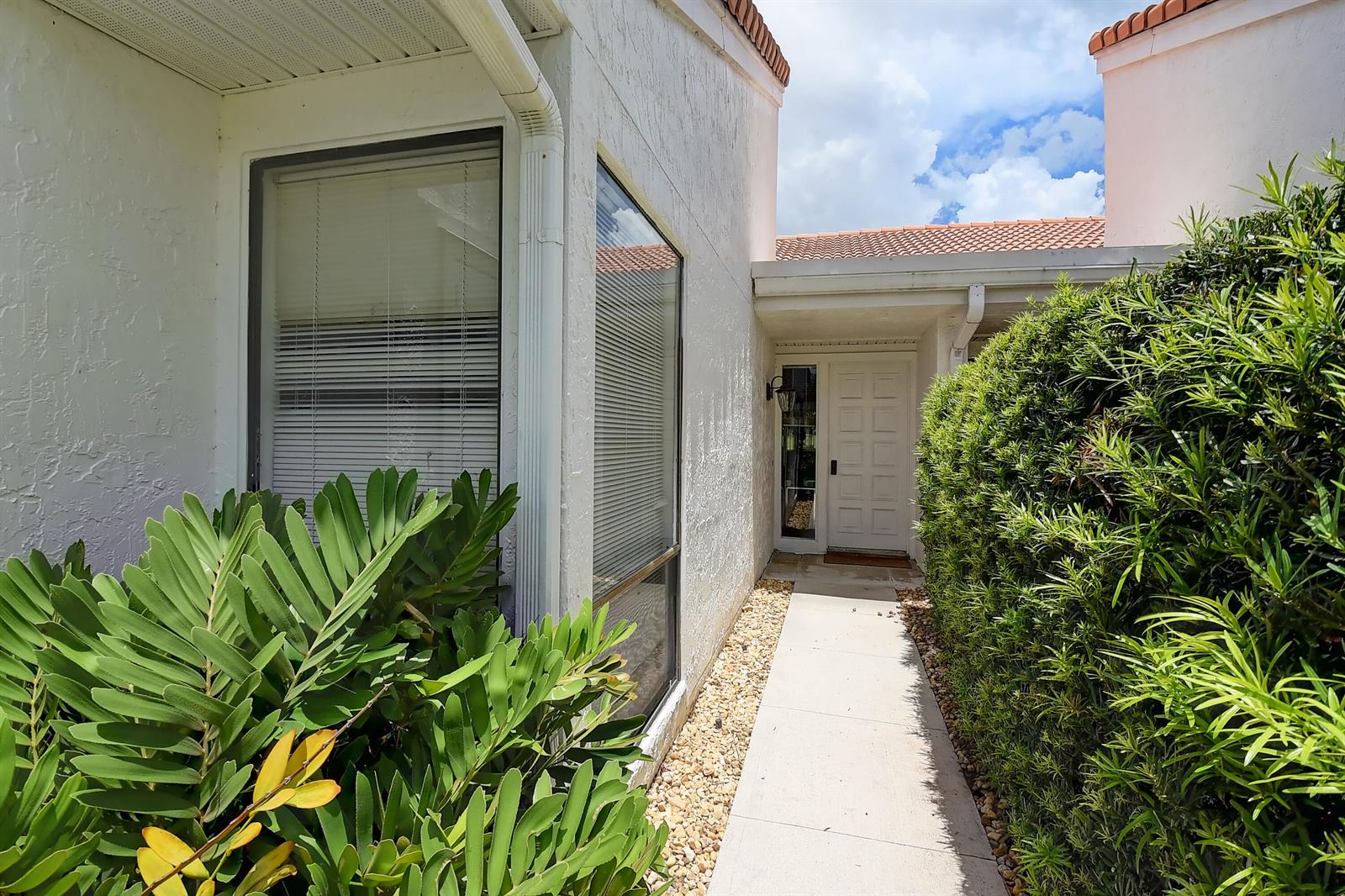 A concrete walkway leads to a white front door flanked by a large window and hedges — 19550 Sawgrass Drive # 2102, Boca Raton FL 33434, BOCA RATON, FL