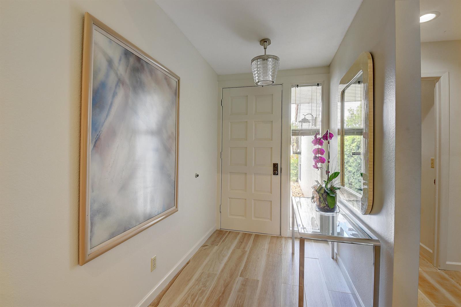 A bright entryway features light wood-look flooring, a glass console table, and a large wall mirror — 19550 Sawgrass Drive # 2102, Boca Raton FL 33434, BOCA RATON, FL