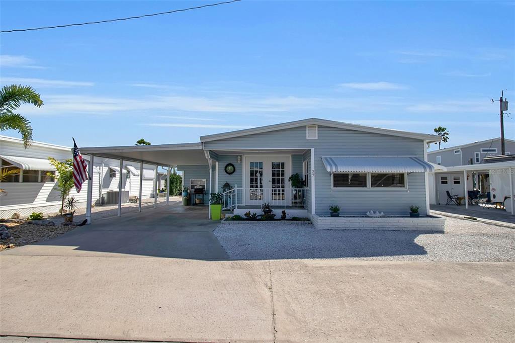 A light blue manufactured home features a carport, a white front door, and gravel landscaping — 10315 CORTEZ ROAD W UNIT 27F, BRADENTON, FL