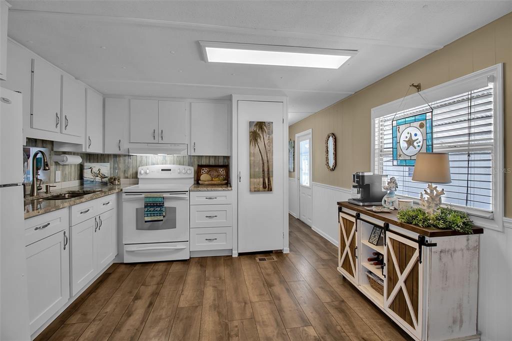 A kitchen features white cabinets, wood-look flooring, a white stove, and a rustic sideboard — 10315 CORTEZ ROAD W UNIT 27F, BRADENTON, FL