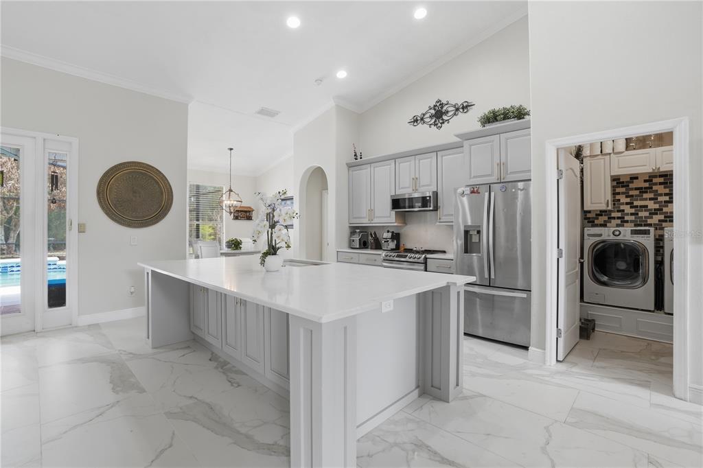 A modern kitchen features a large white island, grey cabinetry, stainless steel appliances, and tile flooring — 510 SONATA COURT, WINTER SPRINGS, FL