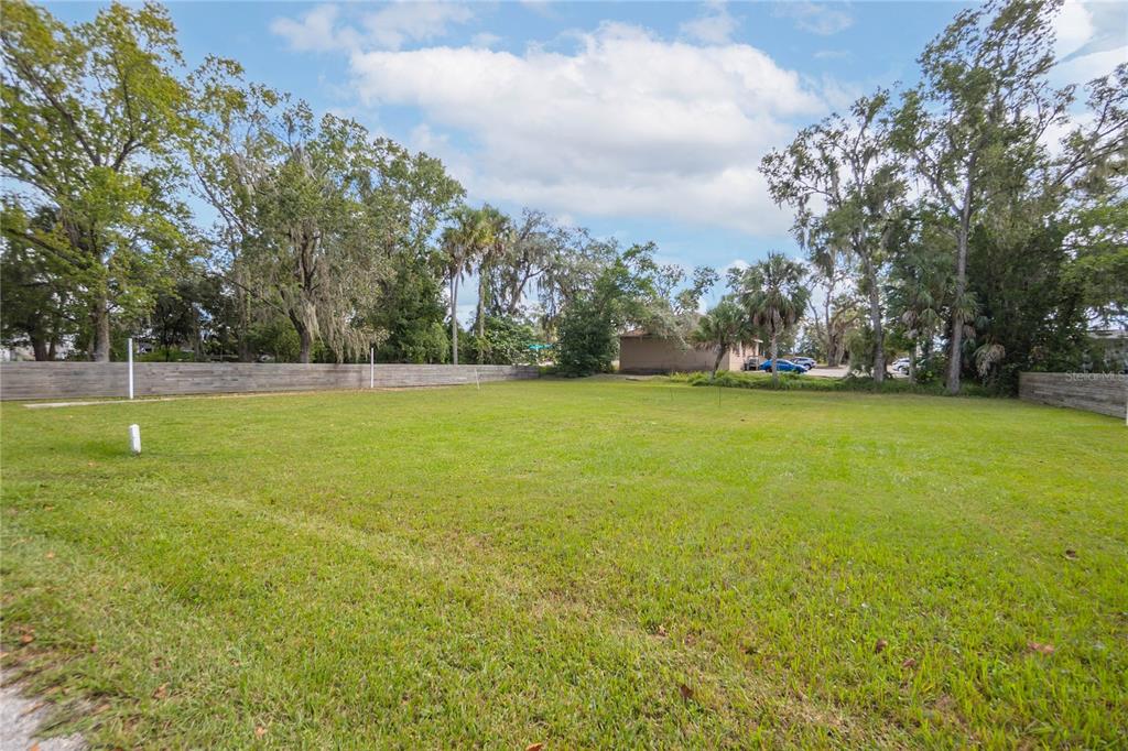 A flat, grassy vacant lot is enclosed by a wooden fence with trees in the background — 464 NE 2ND STREET, CRYSTAL RIVER, FL