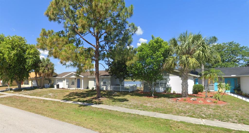 A street view of two single-story houses with lawns, trees, and a glimpse of water — 957 FLORIDA PARKWAY, KISSIMMEE, FL