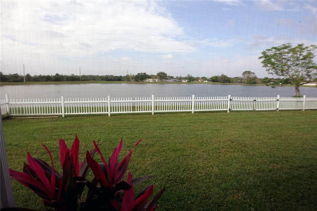 A view of a grassy backyard, white fence, and lake seen through a screen enclosure — 957 FLORIDA PARKWAY, KISSIMMEE, FL