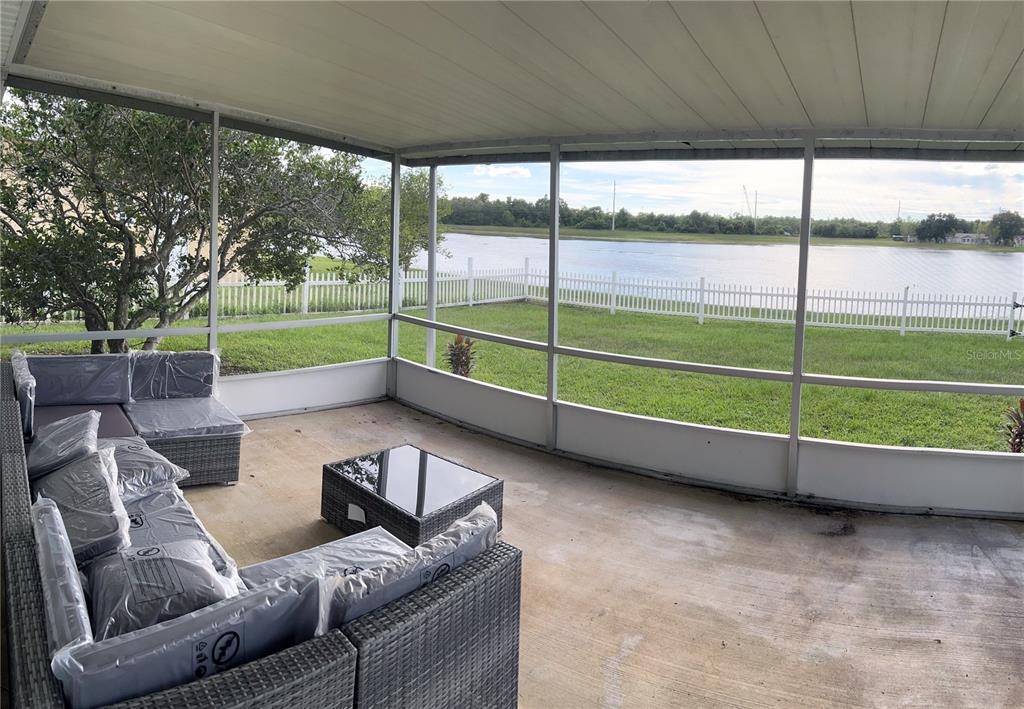 A screened-in patio features wicker furniture and a view of a lake and lawn — 957 FLORIDA PARKWAY, KISSIMMEE, FL