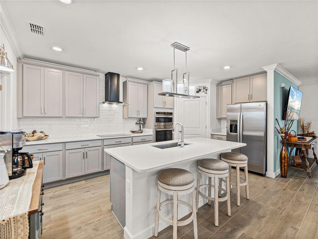 A modern kitchen features light gray cabinets, a white quartz island, and stainless steel appliances — 17319 HOLLY WELL AVENUE, WIMAUMA, FL