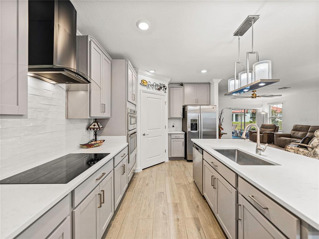 A modern kitchen features gray cabinets, white countertops, stainless steel appliances, and a central island — 17319 HOLLY WELL AVENUE, WIMAUMA, FL