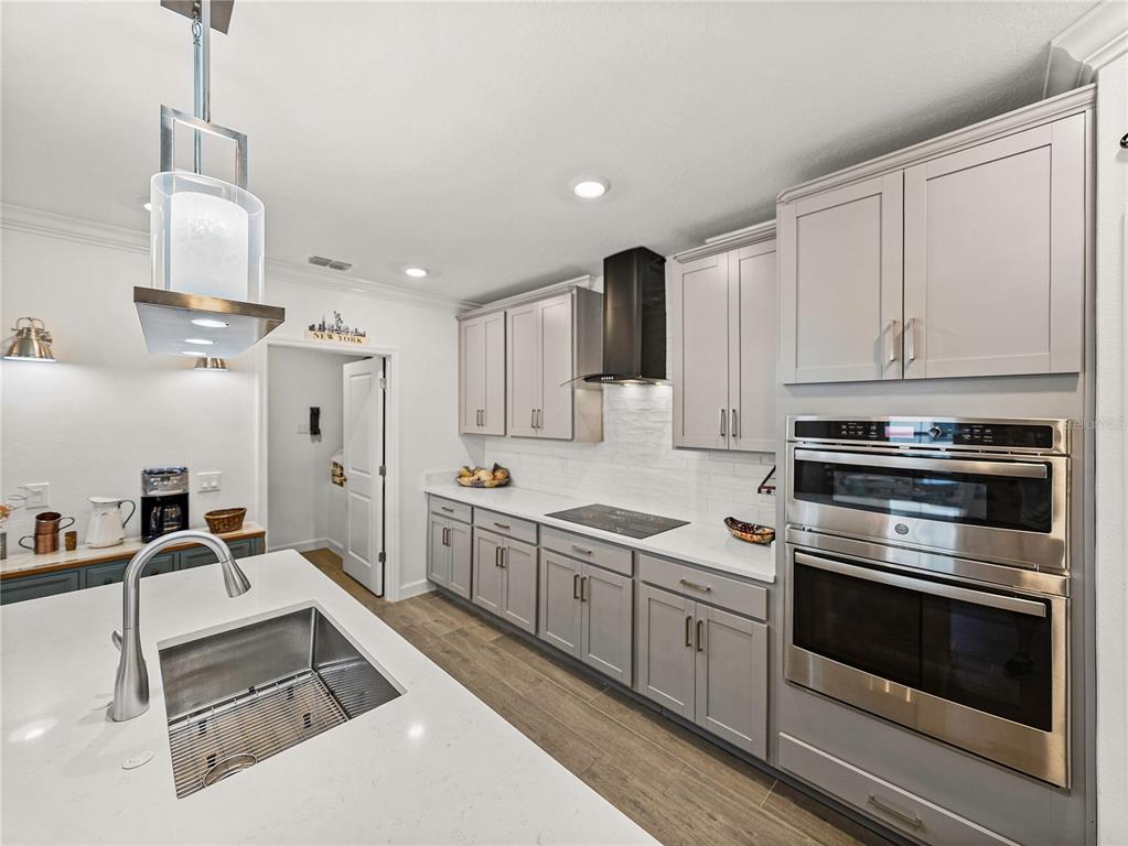 A modern kitchen features gray cabinets, white countertops, stainless steel appliances, and a central island — 17319 HOLLY WELL AVENUE, WIMAUMA, FL