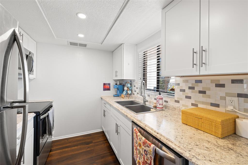 A kitchen features white cabinets, stainless steel appliances, a black refrigerator, and a tiled backsplash — 402 TARPON POINT, TARPON SPRINGS, FL