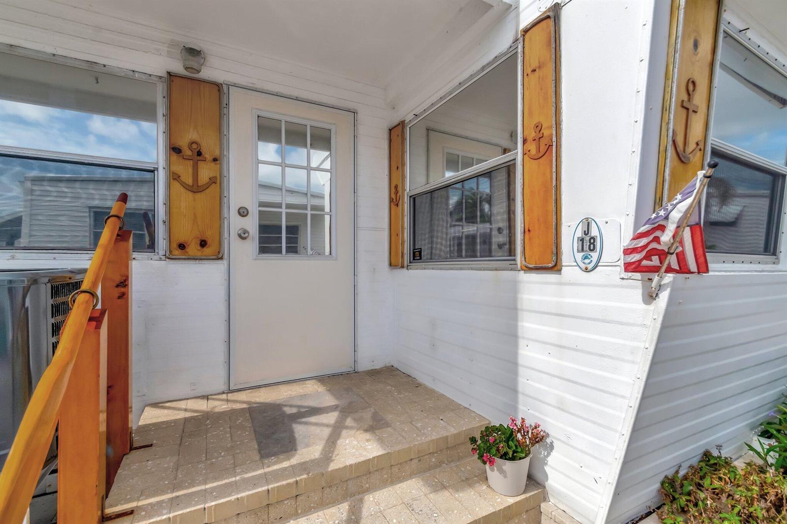 A white exterior entrance with a brick stoop, wooden shutters with anchor cutouts, and flag — 18 Juniper Drive # J, Briny Breezes FL 33435, BRINY BREEZES, FL