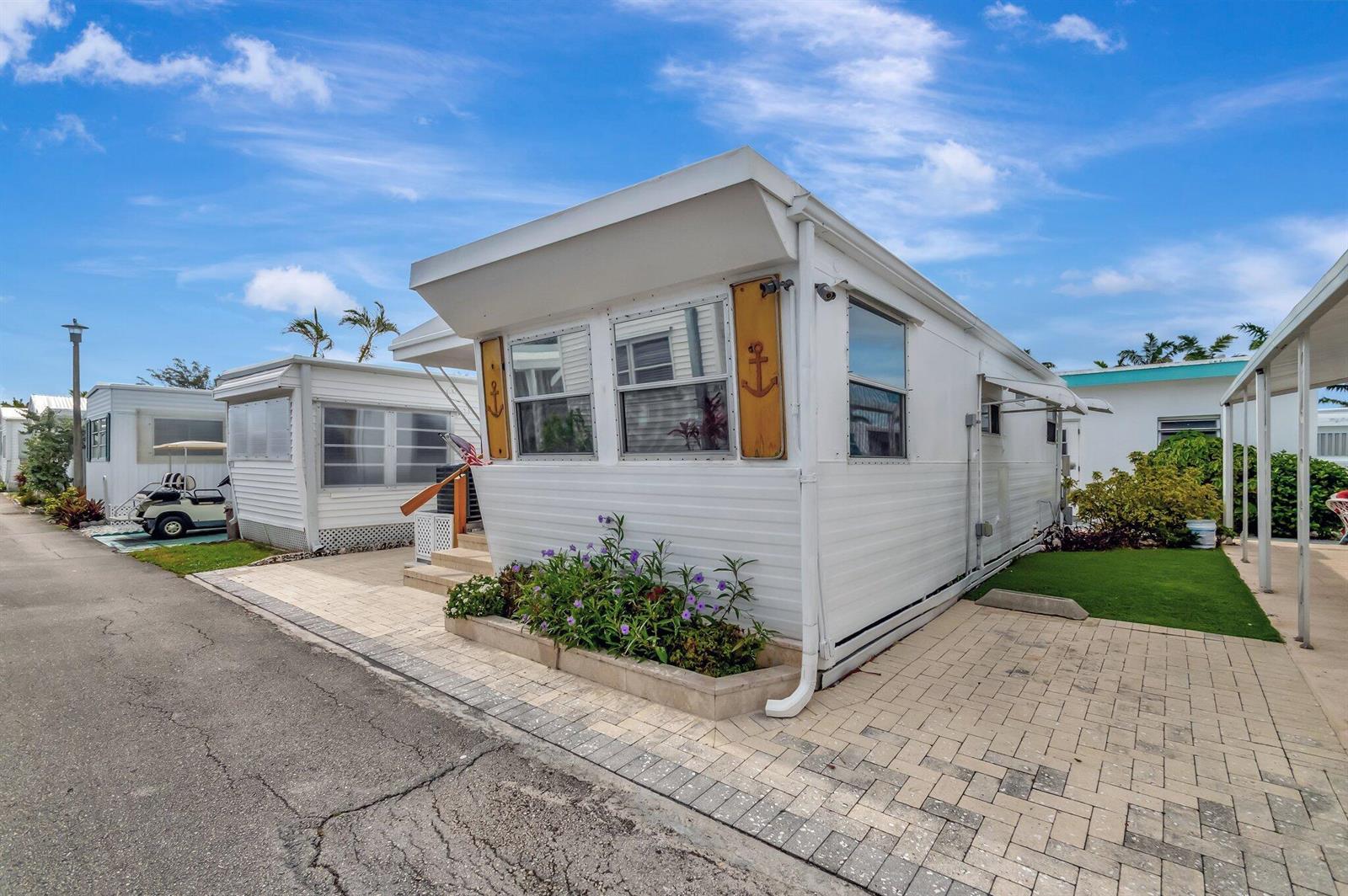 A white mobile home with anchor decor and a paved driveway under a blue sky — 18 Juniper Drive # J, Briny Breezes FL 33435, BRINY BREEZES, FL
