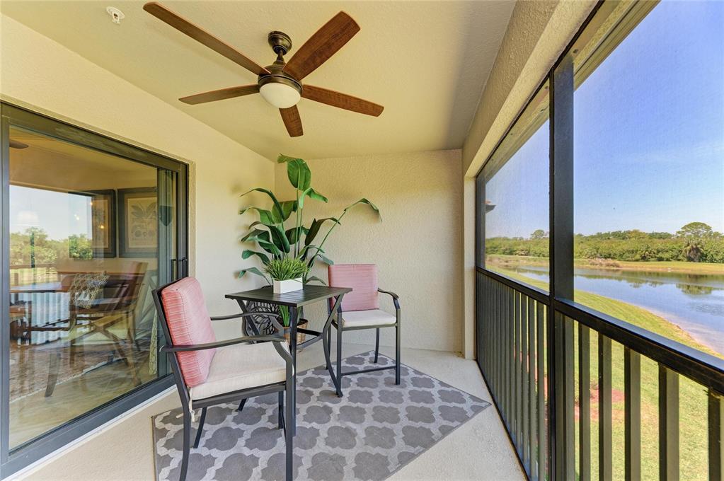 A screened-in balcony features a ceiling fan, a small dining set, and a water view — 6819 GRAND ESTUARY TRAIL UNIT 205, BRADENTON, FL