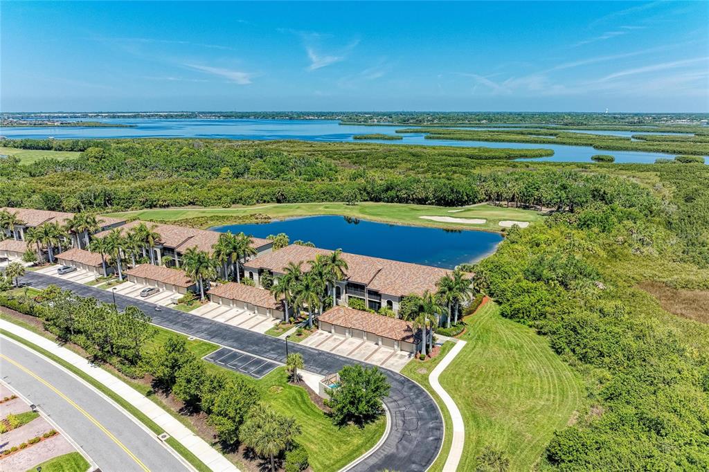 An aerial view shows a multi-unit residential building with garages beside a pond and greenery — 6819 GRAND ESTUARY TRAIL UNIT 205, BRADENTON, FL
