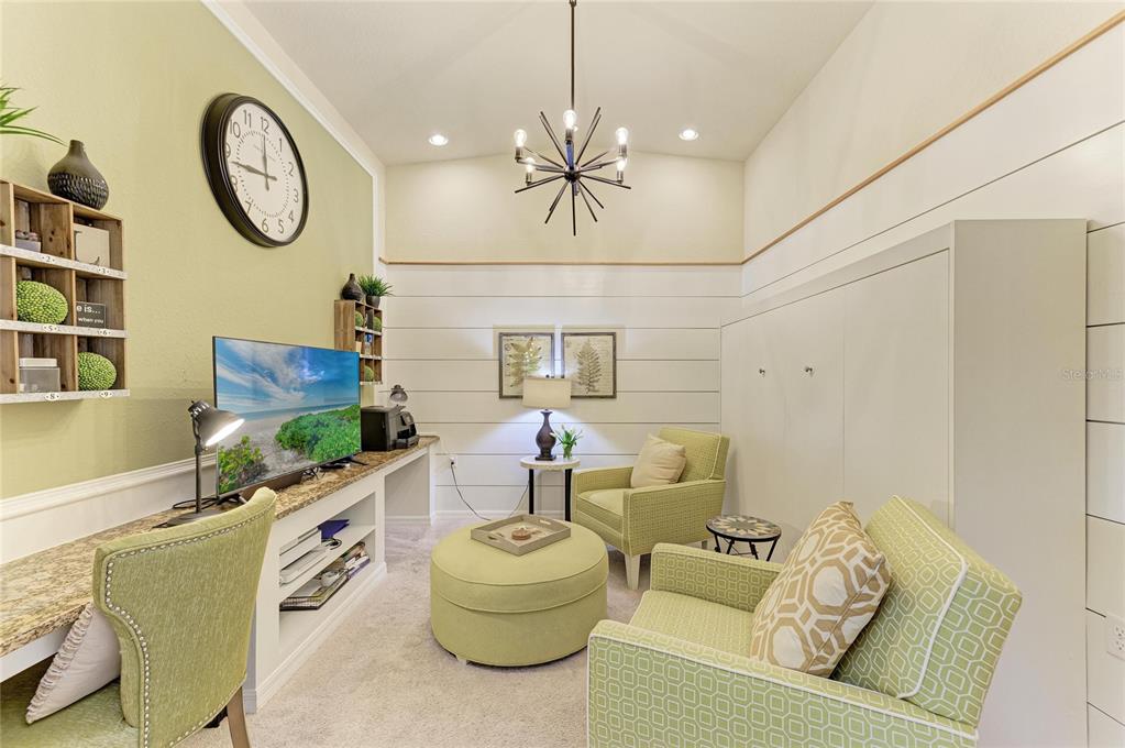 A living room features a desk, television, armchairs, an ottoman, and white shiplap walls — 6819 GRAND ESTUARY TRAIL UNIT 205, BRADENTON, FL