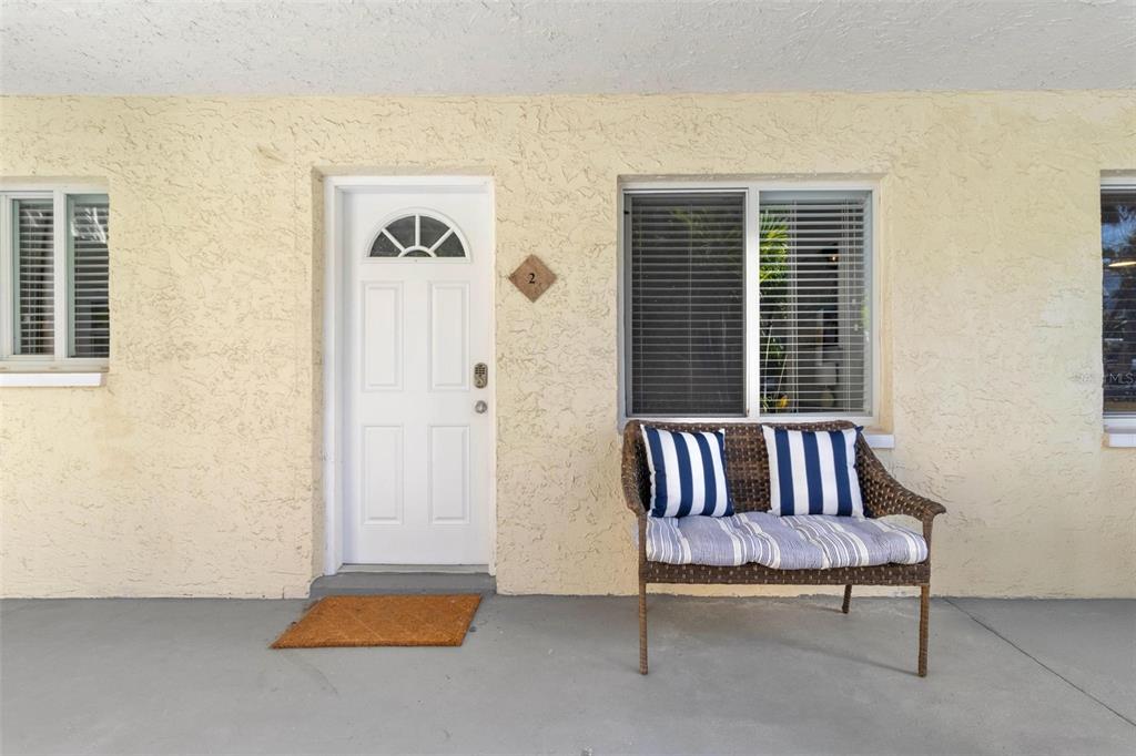 A white front door and a wicker bench sit on a concrete porch — 2704 2ND STREET UNIT 2, INDIAN ROCKS BEACH, FL