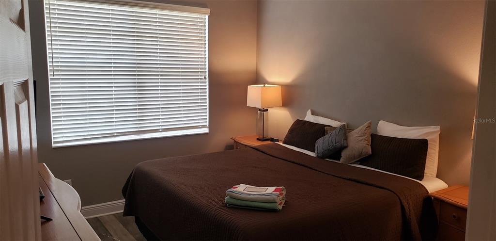 A bedroom features a bed with a brown quilt, two nightstands, and a window with blinds — 21032 PICASSO COURT UNIT 205, LAND O LAKES, FL
