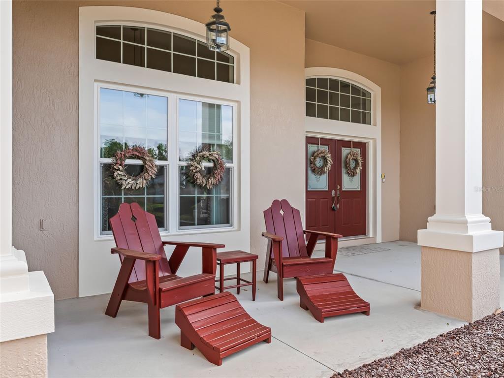 A covered front porch features two red Adirondack chairs with matching ottomans and double doors — 8755 SE 177TH GRASSMERE STREET, THE VILLAGES, FL